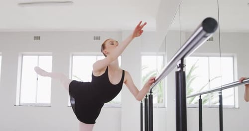 Caucasian female ballet dancer stretching up by the mirror in a bright studio