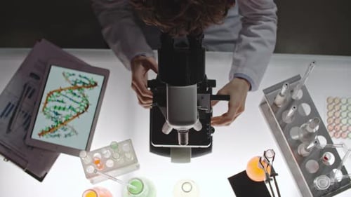 Scientist Adjusting Microscope With DNA Tablet Nearby
