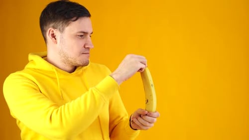 Close Up of Young Man Peeling Banana on Yellow Background