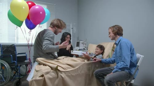 Side View, Relatives Give a Present To Girl Who Lie on the Bed in the Hospital