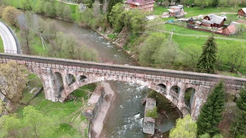 Aerial view of old railroad viaduct bridge over river in mountains.