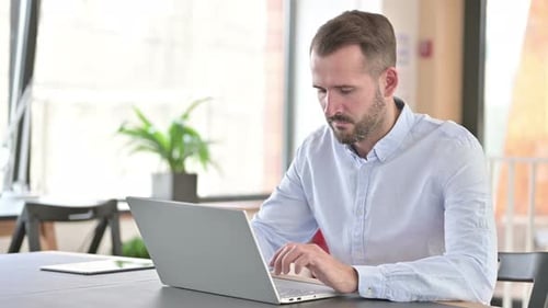 Young Man with Laptop Doing Thumbs Up in Office