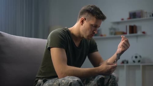 Contemplative Man Holding Military Dog Tags on Couch