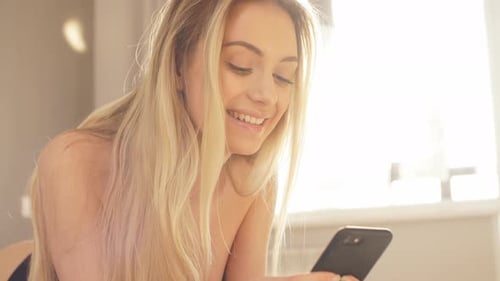 Woman on Bed Uses Phone and Smiles