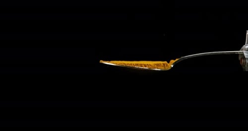 Spoon and Curry Powder falling against Black Background, Slow motion 4K