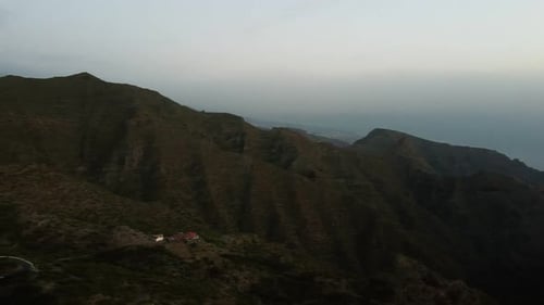 Aerial Flight Over Serpentine Road Beyound Mountains Covered with Green Forest