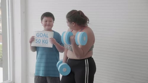 Asian family with mother in sportswear lifting dumbbell and son cheer with goal for diet.