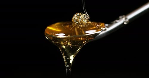 Honey Flowing on Spoon against Black Background, Slow Motion 4K
