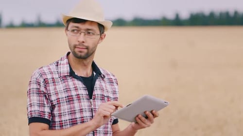 Farmer Uses a Tablet Stands Against the Background of a Wheat Field