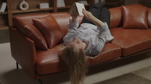 Woman Reads Book Reclined on Brown Couch