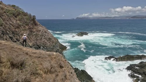 Endless Sea Horizon and Woman on Top of Cliff with Strong Waves Crashing