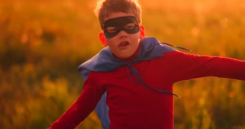 Boy in Superhero Costume and Mask Running Across the Field at Sunset Dreaming and Fantasizing