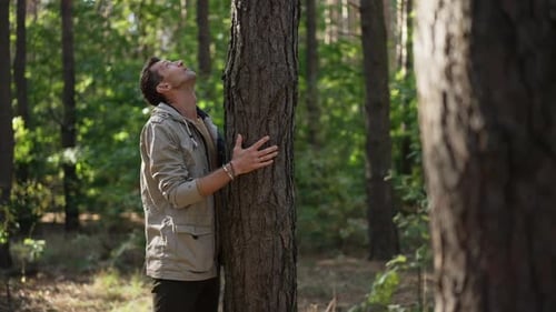 Side View Caucasian Man Standing at Tree Trunk Looking Up in Woodland