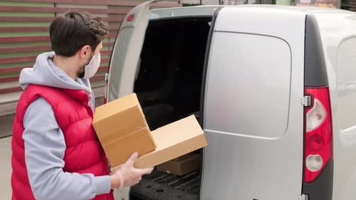 Zusteller mit Gesichtsmaske beim Laden von Paketen in den Van