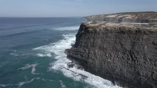 Aerial view of black cliffs in strong waves in