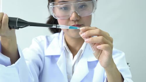 Female Scientist Works with Pipette and Blue Liquid
