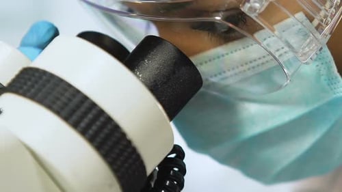 Scientist Looking Through Microscope Wearing Mask and Goggles