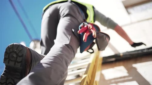 Pull-out downwards shot of a fiber optics technician wearing protective gear going down a ladder