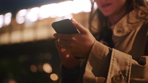 Young woman in the city holding her phone and typing at night