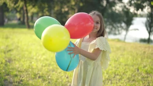 Positive Girl Playing with Multicolored Balloons on Sunny Day in Spring Summer Park