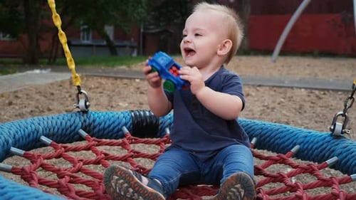 Happy Baby Boy Plays on Playground Swing
