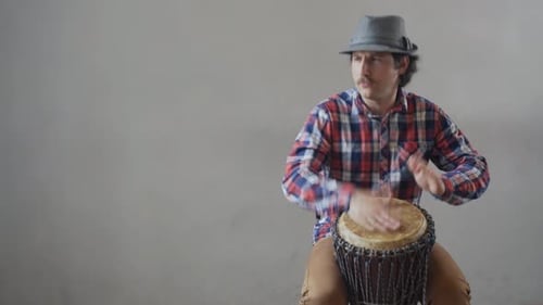 Funny Man with a Mustache and a Hat Playing the Ethnic Drum
