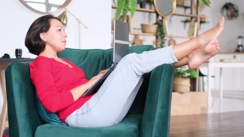 Woman Relaxes in Chair While Working on Laptop