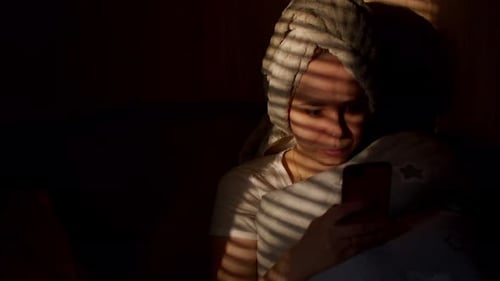 Close Up of Young Woman with Towel on Her Head Browsing Smartphone in Dark Room
