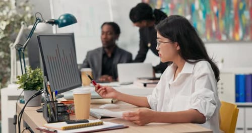 An Attractive Girl Wearing Glasses Works at a Desk in Front of a Computer Fills Out Documents Signs