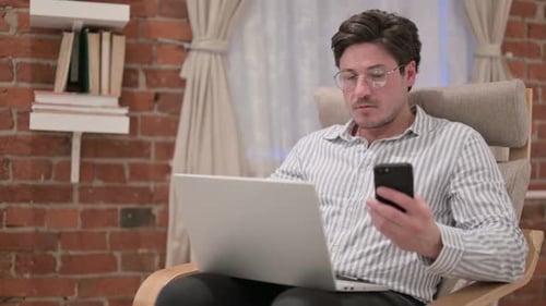 Man Uses Laptop and Phone in Chair