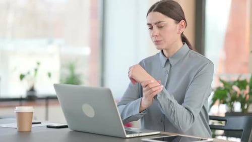 Woman Massaging Wrists While Working on Laptop
