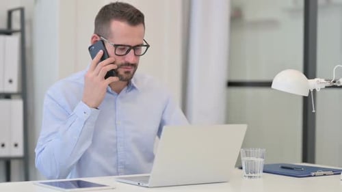 Man Answers Phone at Desk at Bright Office