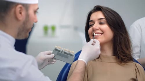 Male Doctor Choosing Color of Teeth Trying on Female Patient at Modern Clinic