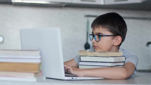 Attraktiver Schüler macht Hausaufgaben, während er in der Küche am Tisch sitzt und viel benutzt