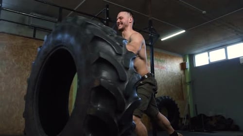 Confident Strong Man Flipping Big tire During Training in the Gym