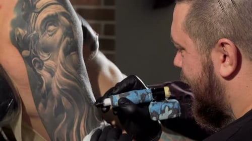 Rear View Shot of a Tattoist Making Tattoos on the Arm of Male Client