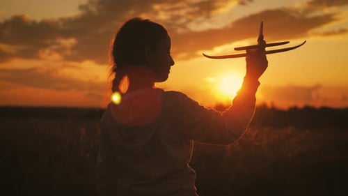 Cute Girl Playing with Toy Airplane in the Wheat Field at Sunset. Silhouette of Child Playing with