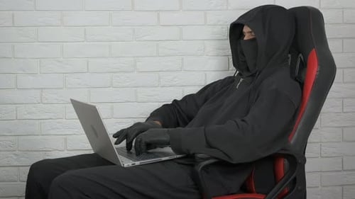 Hooded Man Typing on a Laptop in a Chair