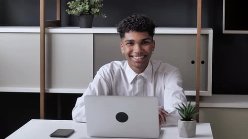 Young African Student Male Working on Computer at Office. Sitting at the Table Waving at the Camera