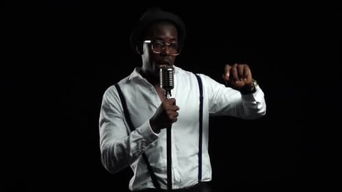El cantante canta en un micrófono girando, saltando y bailando a su alrededor. Fondo negro. Lento