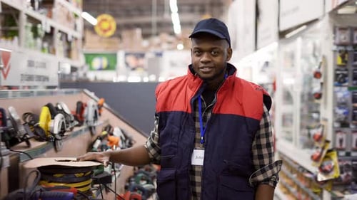 Smiling Salesman Standing Between Rows in Hardware Store Looking to the Camera