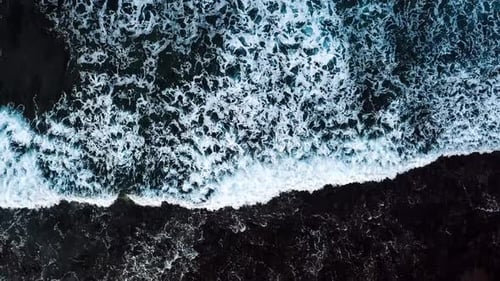 Above vertical view of blue ocean waves and black rocks coast - summer holiday vacation