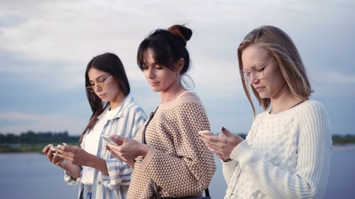 Three Women Using Phones Outside by River