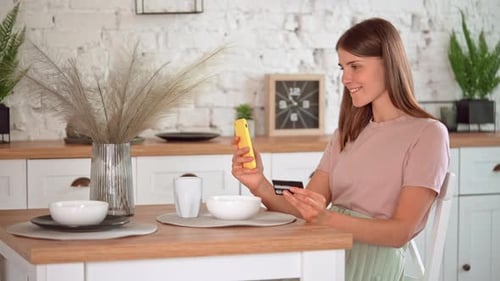 Woman Using Phone and Credit Card in Kitchen