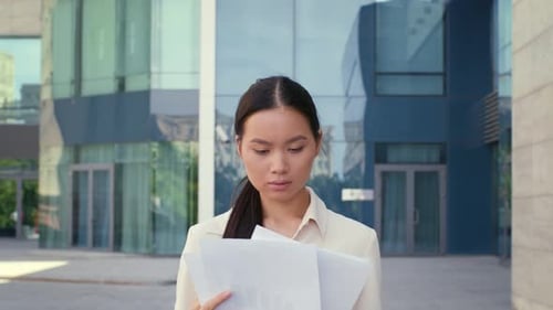 Confident Asian Businesswoman Reading Papers And Documentation Walking Outdoors