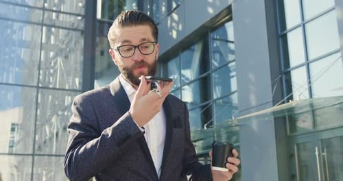 businessman which holding cup of coffee and talking on phone near modern glass building