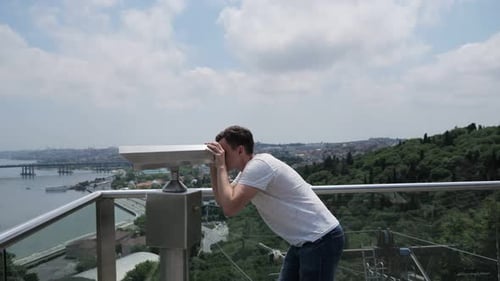 Mann schaut durch ein Fernglas und steht auf der Aussichtsplattform