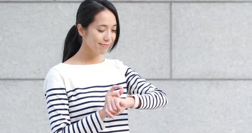 Woman Interacts with Smartwatch Against City Wall