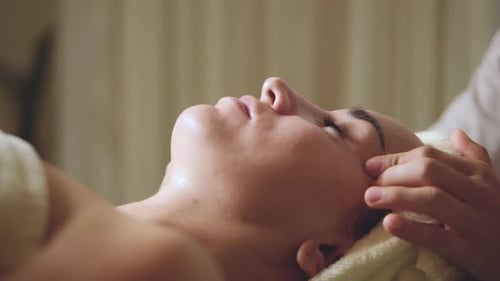 Nahaufnahme einer jungen Frau mit einem Handtuch auf dem Kopf erhalten eine Gesichtsmassage und eine Spa-Behandlung für