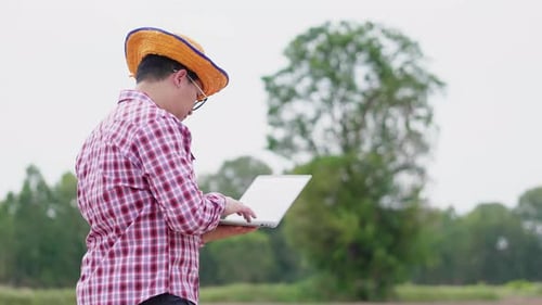 Asiatischer Bauer steht und arbeitet am Laptop auf der Farm